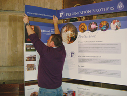 Frère Ray Dwyer, F.P.M. affiche un placard de publicité vocationnelle pour les Presentation Brothers.
